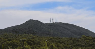 Serra do Elefante em Mateus Leme, com vegetação nativa, torres de telefonia no alto e céu nublado