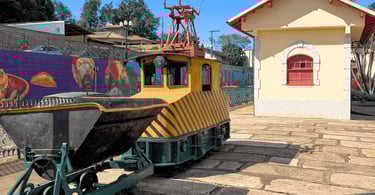 Museu Ferroviário de Itabirito MG com locomotiva antiga, mural colorido e prédio histórico ao lado