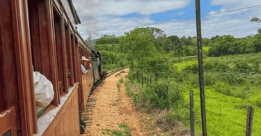 Janela de trem de madeira emoldurando a vista de campos verdes e morros em Tiradentes