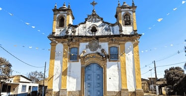 Vista frontal da Igreja Matriz de Itatiaia, com cores brancas e amarelas, portas e janelas azuis