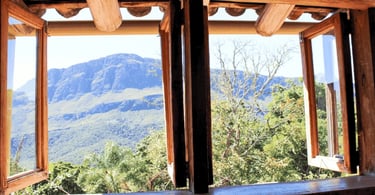 Vista das montanhas de Itatiaia MG pela janela de uma casa rústica, cercada por natureza verde