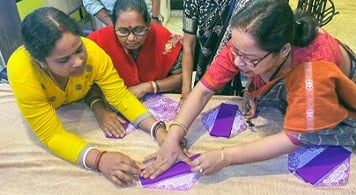 Three women discussing how to make fabric sanitary napkins