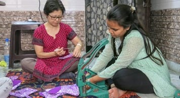 Two women using a snap machine to put snaps onto fabric sanitary napkins.