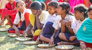 6 girls sitting on grass eating from plates of food on grass.