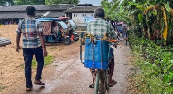 2 men  one walking and one cycling, on narrow gravel road approaching school.