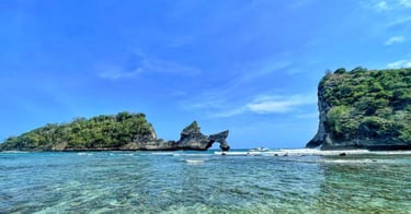 two women walking into turquoise ocean on a white sandy beach with limestone cliffs and lush green islands under blue sky