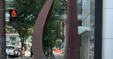A large oval metal sculpture stands on a modern city sidewalk in Calgary depicting Identity & Worth!