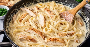 Homemade Alfredo sauce being stirred in a skillet with sliced chicken and cooked fettuccine.