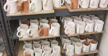 Shelves full of glazed slab mugs waiting to be fired.