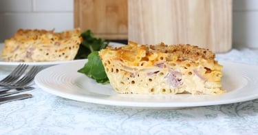 Slice of baked macaroni and cheese casserole with ham and breadcrumb topping on a white plate.