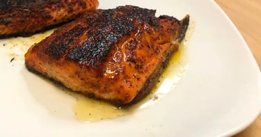 Blackened steelhead trout on a white plate topped with lemon garlic butter sauce