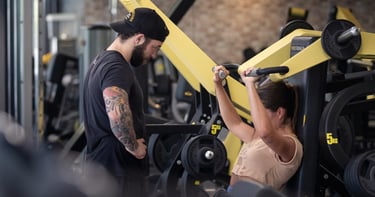 moi en train de coacher ma cliente emmie sur une shoulder press tecnogym