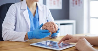 Close-up of a neurology provider holding a brain model and using a tablet to explain diagnosis and lifestyle factors to a pat