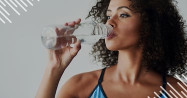 A curly-haired woman in fitness apparel drinking fresh water from a bottle to stay hydrated.