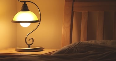 Vintage wrought iron bedside lamp with warm glow on a wooden nightstand next to a bed.