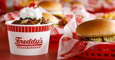 Freddy's Frozen Custard turtle sundae with whipped cream and a cherry next to a steakburger.