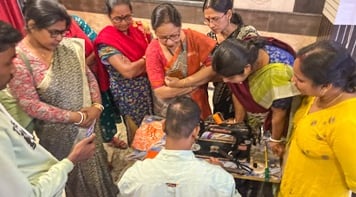 Eight women standing looking down at a sewing machine and fabric