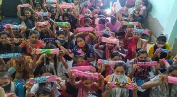 Thirty girls in a small classroom holding up Hanaru's sanitary napkins.