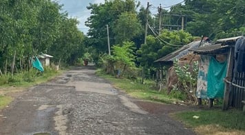 Partly paved country road  in West Bengal with small lean-to buildings at the side.
