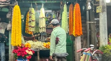 Man outside stall selling flower malas, used for ritual. Yellow cream and orange flowers.