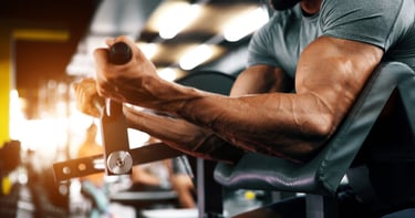 Muscular man performing bicep curls on a preacher curl machine in a modern gym setting.
