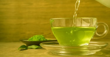 Té verde vertiéndose en una tasa de crista, con polvo de te matcha y hojas de té verde