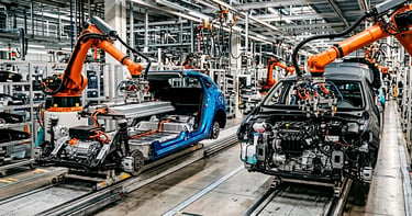 Línea de montaje con coche eléctrico y otro de gasolina, mostrando estrategias divergentes