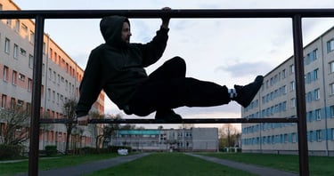 A man in a green hoodie performs parkour moves on a metal frame in an urban residential courtyard.