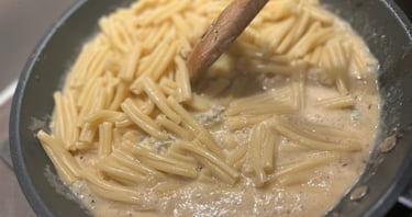 Cooking short pasta in a creamy sauce being stirred with a wooden spoon in a non-stick frying pan.