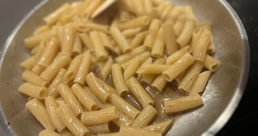 Rigatoni pasta cooking in a stainless steel skillet with butter sauce and pepper.