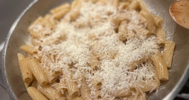 Rigatoni pasta with grated Pecorino cheese and black pepper in a stainless steel pan.