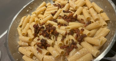Rigatoni pasta alla Gricia with crispy guanciale and creamy egg sauce in a stainless steel pan.