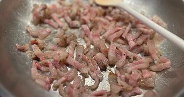 Slicing and browning guanciale or pancetta strips in a stainless steel skillet with a wooden spoon.