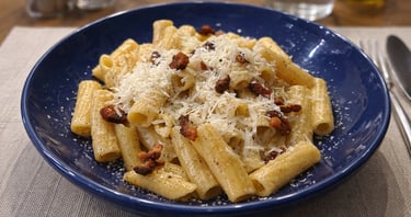 Rigatoni alla Gricia pasta with crispy guanciale and pecorino cheese in a blue bowl.