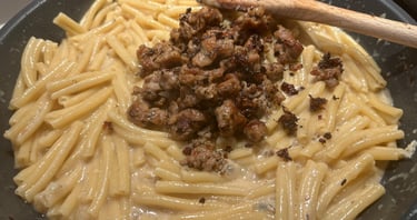 Creamy pasta with browned Italian sausage in a skillet being stirred with a wooden spoon.