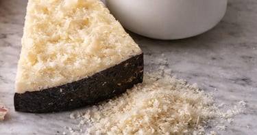 Wedge of hard aged Pecorino cheese with black rind and grated shavings on a marble countertop.