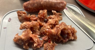 Fresh raw Italian salsiccia sausage removed from casing on a cutting board with a kitchen knife.