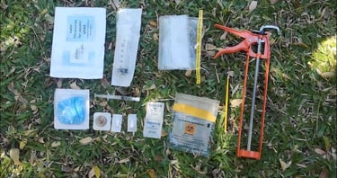 Field eDNA water filtration kit with syringe, parafilm, and sampling tools on grass.