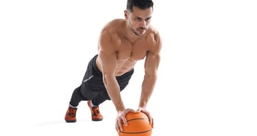 Muscular man performing a medicine ball plank for core strength and stability on a white background.