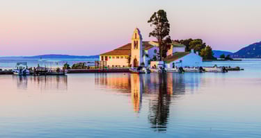 Vista do passeio de barco em Corfu, com a igreja no mar ao fundo e barcos ancorados no pier.