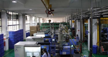 Industrial factory floor featuring rows of plastic injection molding machines and blue storage bins.