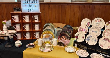 Vintage-style sweary sassy china plates and mugs displayed at a craft fair market stall.