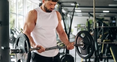 Muscular man performing bicep curls with an EZ curl barbell during a workout in a gym.