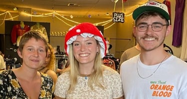 Three smiling friends posing at a vintage clothing store or thrift shop.