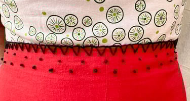 Embroidered waist of a white, green, and red strappy sundress