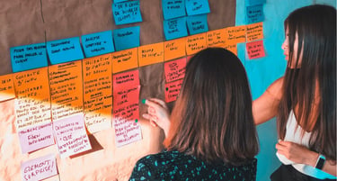 Two people brainstorming and writing on colorful sticky notes and a whiteboard, showcasing collaborative business strategy