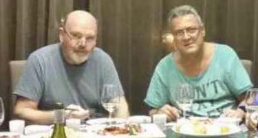 Two men enjoy a casual dinner with wine and shared appetizers at a restaurant table.