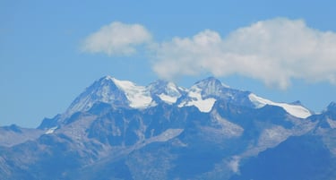 Snow-capped mountain peaks of the Andes range under a clear blue sky with fluffy white clouds.