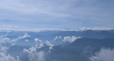 Panoramic view of blue mountain ranges and misty valleys under a bright sky with wispy clouds.