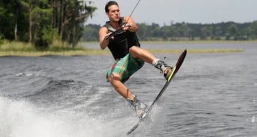 A man in a life jacket performing an athletic jump while wakeboarding on a lake.